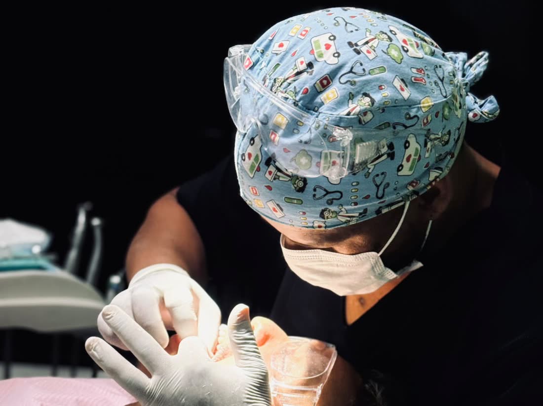 Dentista da Sorrir Bem, de touca estampada, óculos de proteção e máscara, atende uma paciente na cadeira odontológica